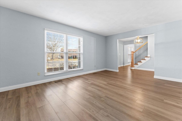 empty room featuring visible vents, baseboards, wood finished floors, and stairs