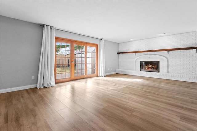 unfurnished living room featuring wood finished floors, baseboards, brick wall, a fireplace, and french doors