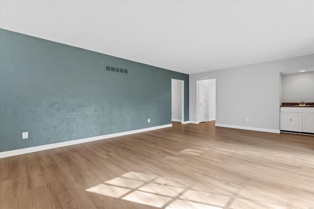 unfurnished living room with visible vents, wood finished floors, baseboards, and a sink