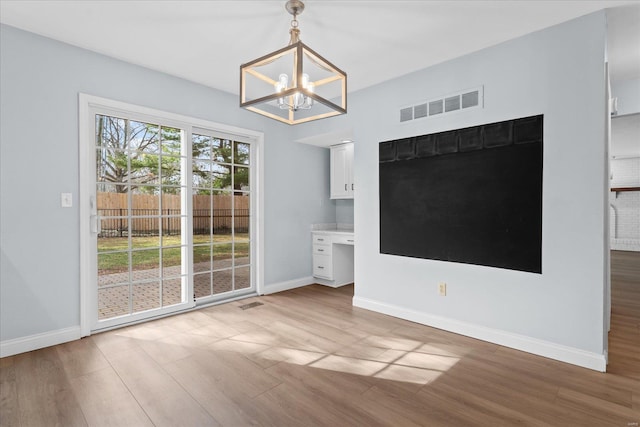 unfurnished dining area with visible vents, light wood finished floors, baseboards, and built in study area