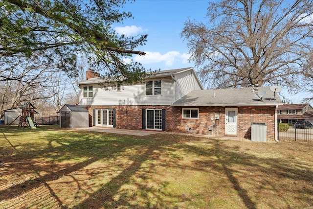 rear view of property with a playground, fence, a lawn, a patio area, and a storage unit