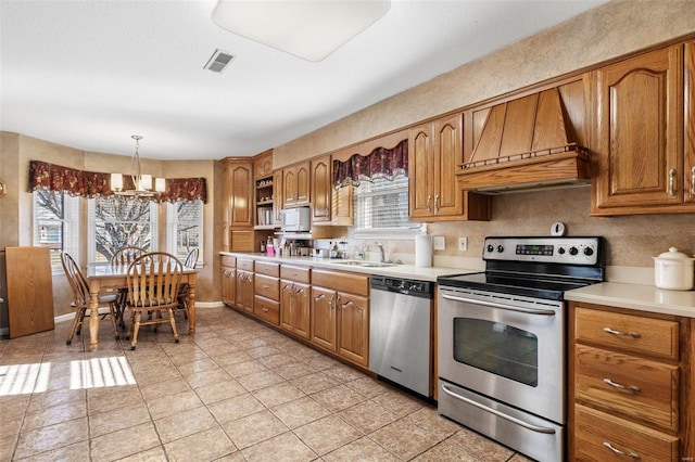 kitchen with brown cabinets, tasteful backsplash, light countertops, appliances with stainless steel finishes, and premium range hood