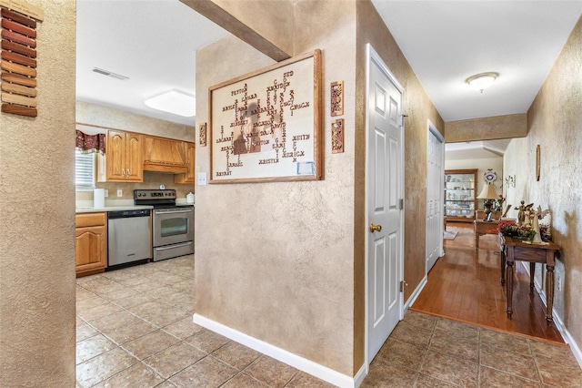 hallway featuring light tile patterned floors, a textured wall, visible vents, and baseboards