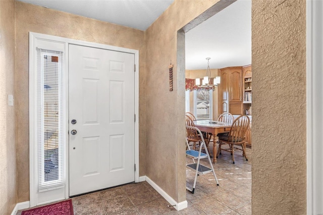 foyer entrance featuring tile patterned flooring, a textured wall, baseboards, and an inviting chandelier