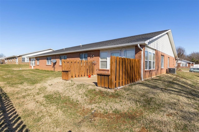 rear view of house featuring brick siding, a yard, and central AC