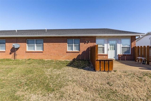 back of house featuring a patio, brick siding, a shingled roof, fence, and a yard