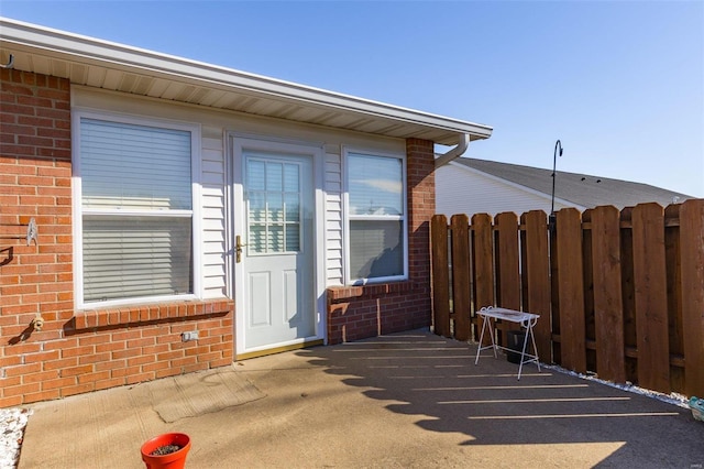 entrance to property featuring fence and brick siding