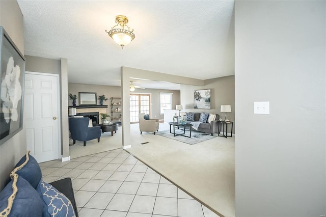 living area featuring a fireplace, light colored carpet, light tile patterned flooring, ceiling fan, and a textured ceiling