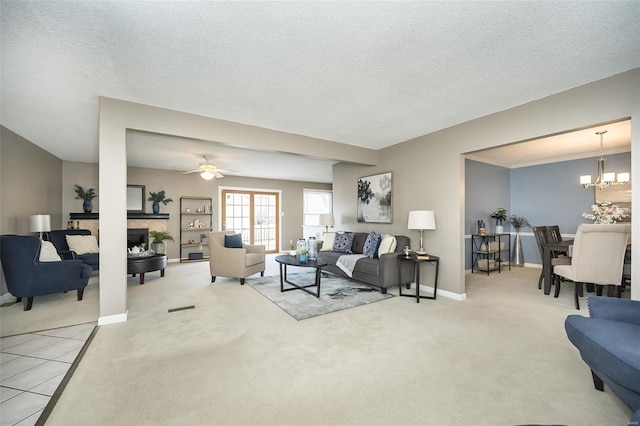 carpeted living area featuring ceiling fan with notable chandelier, baseboards, a textured ceiling, and a stone fireplace