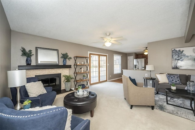 living area with light carpet, ceiling fan, a stone fireplace, a textured ceiling, and baseboards