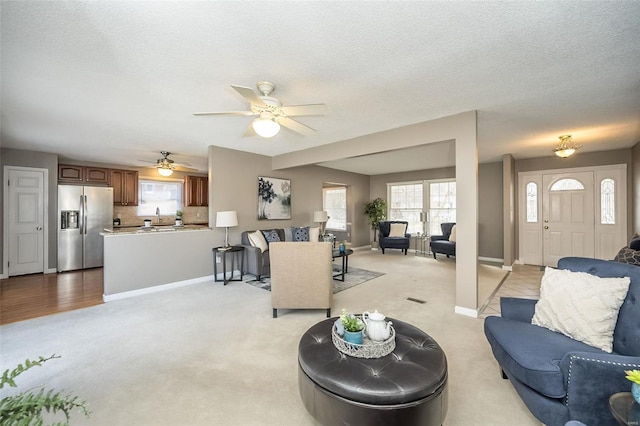 living area with light carpet, a textured ceiling, baseboards, and a healthy amount of sunlight