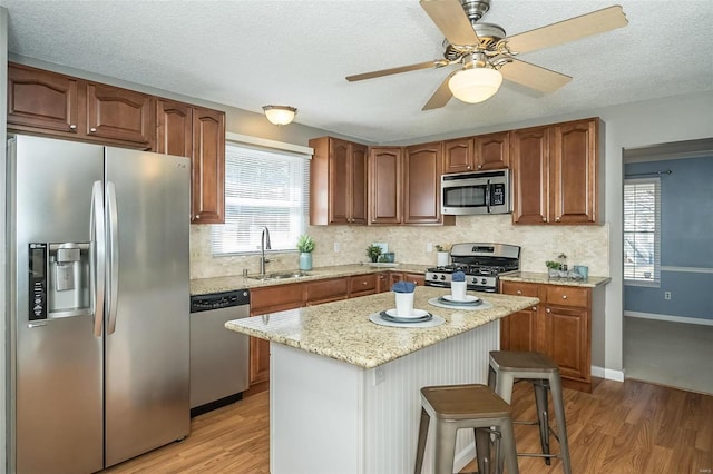 kitchen featuring light wood finished floors, decorative backsplash, light stone countertops, stainless steel appliances, and a sink