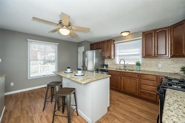 kitchen featuring a breakfast bar area, light wood-style flooring, stainless steel appliances, a sink, and a center island