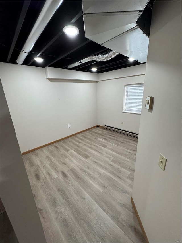 basement with light wood-style flooring, baseboards, and baseboard heating