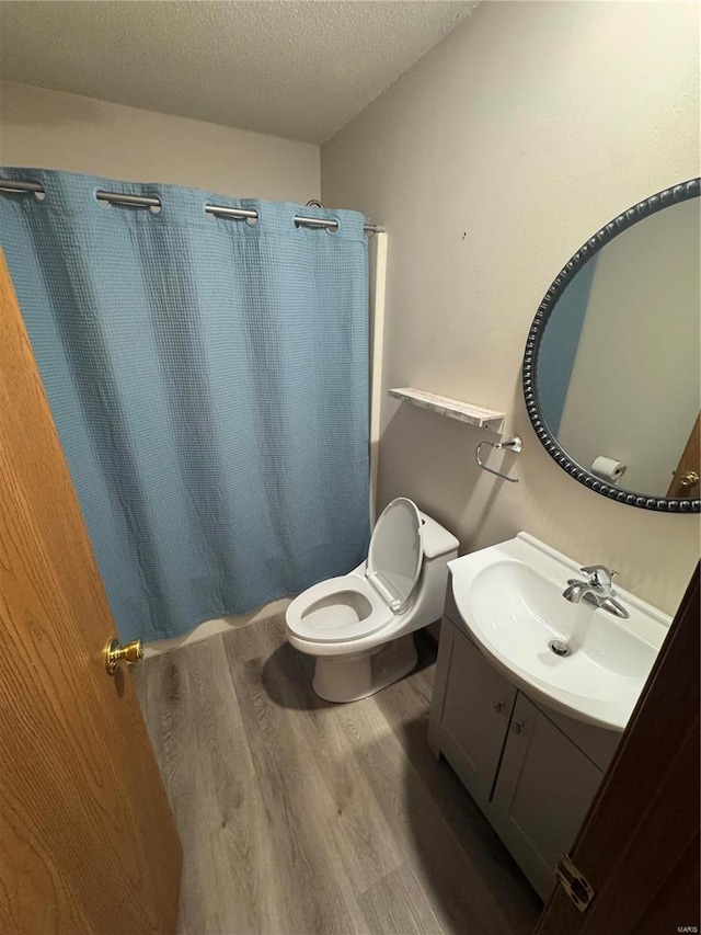 bathroom with a textured ceiling, toilet, a shower with shower curtain, wood finished floors, and vanity