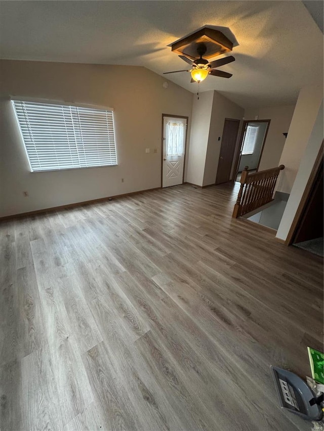 unfurnished living room featuring baseboards, lofted ceiling, ceiling fan, wood finished floors, and a textured ceiling