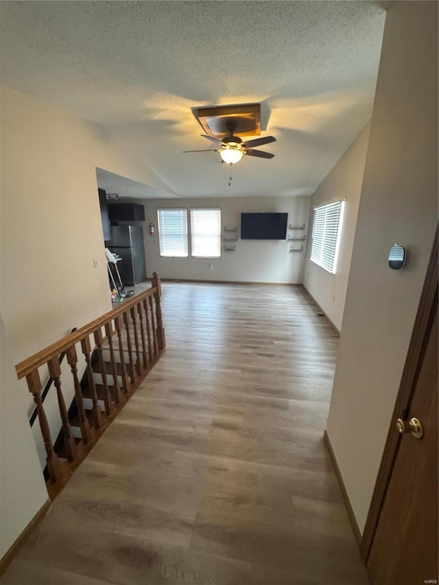 corridor featuring baseboards, a textured ceiling, an upstairs landing, and wood finished floors