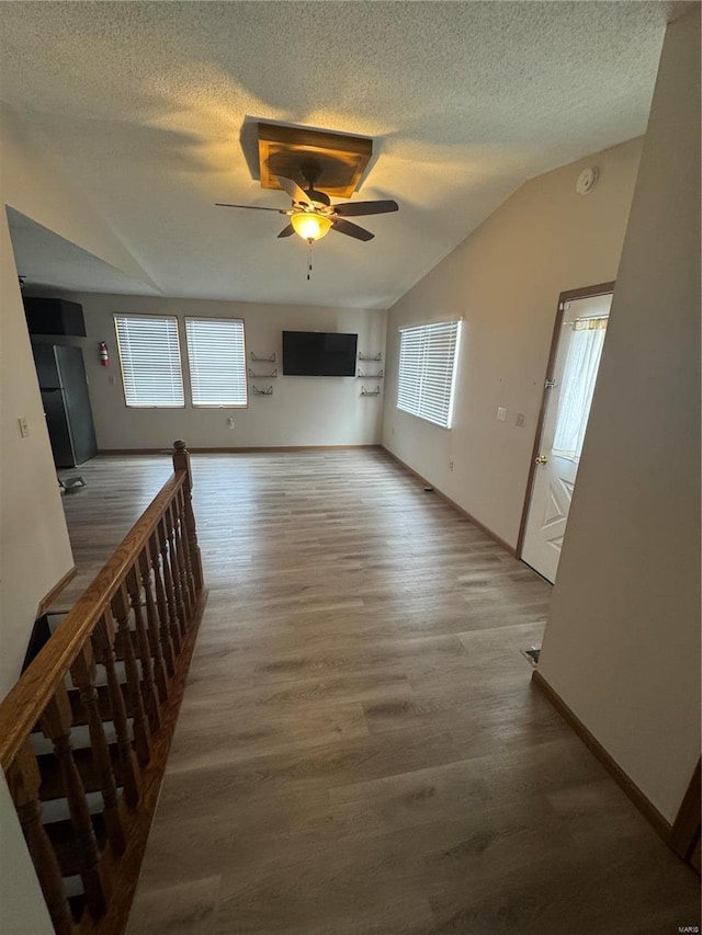 unfurnished living room featuring baseboards, a ceiling fan, wood finished floors, vaulted ceiling, and a textured ceiling