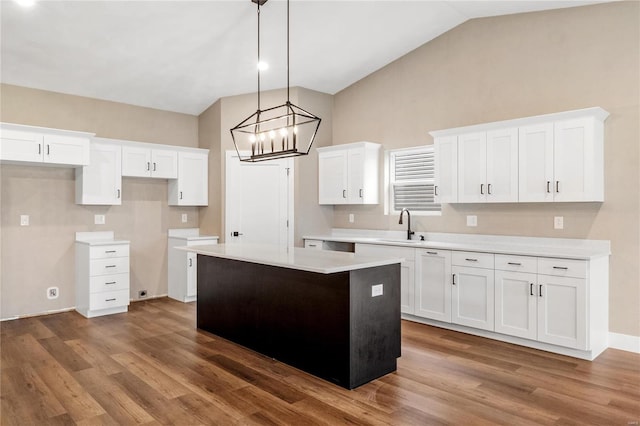 kitchen with wood finished floors, lofted ceiling, a sink, white cabinets, and a center island