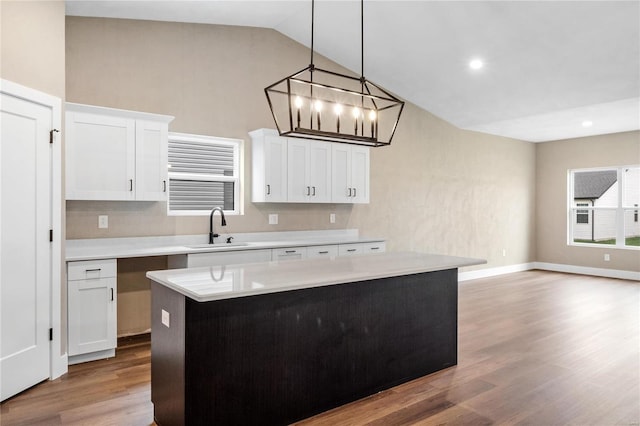 kitchen with a center island, light countertops, wood finished floors, white cabinets, and a sink