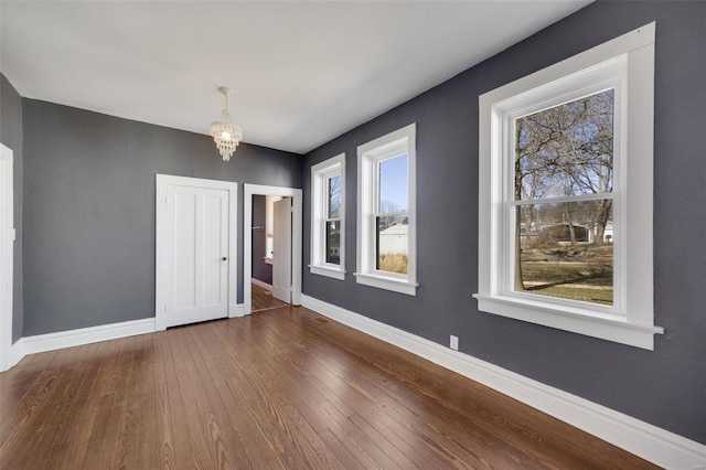 unfurnished room with a chandelier, dark wood-type flooring, and baseboards