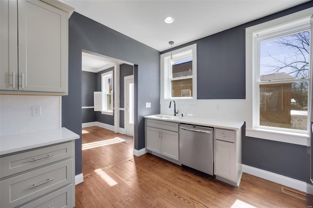 kitchen featuring tasteful backsplash, dishwasher, light countertops, light wood-type flooring, and a sink