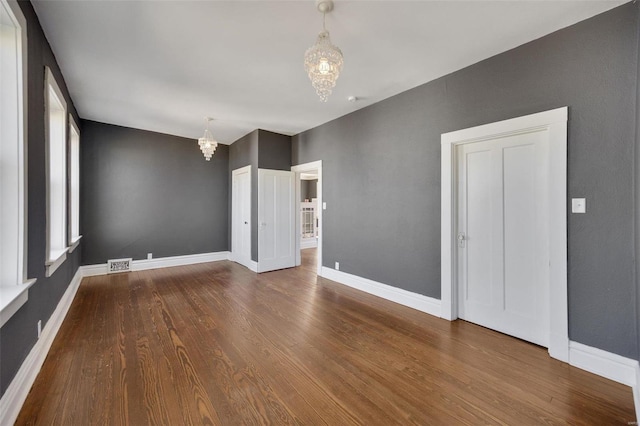 empty room featuring a chandelier, visible vents, baseboards, and wood finished floors