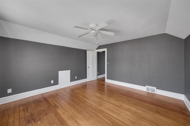 spare room with lofted ceiling, wood finished floors, visible vents, and baseboards