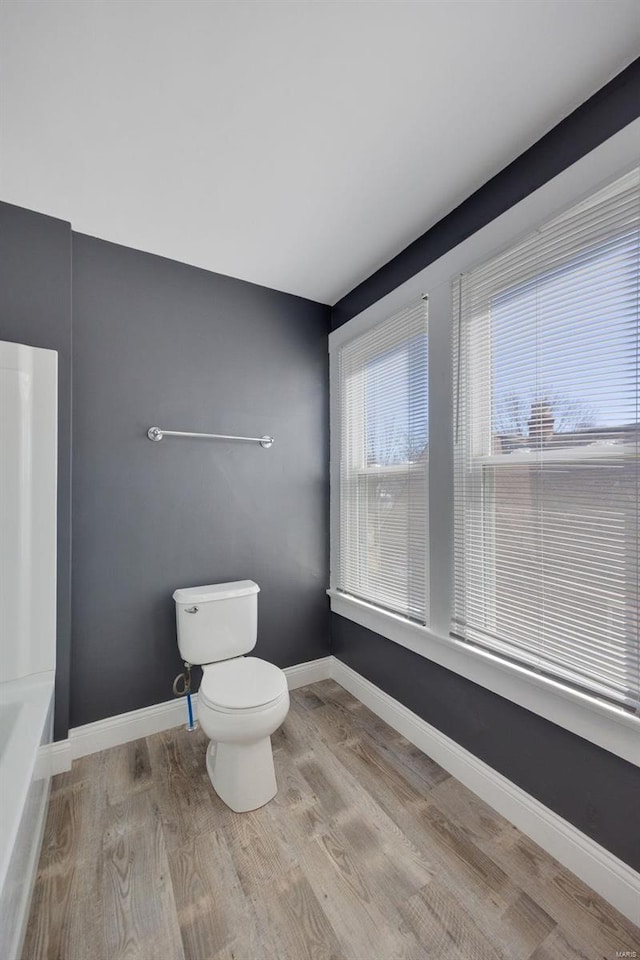 bathroom featuring toilet, a tub, baseboards, and wood finished floors