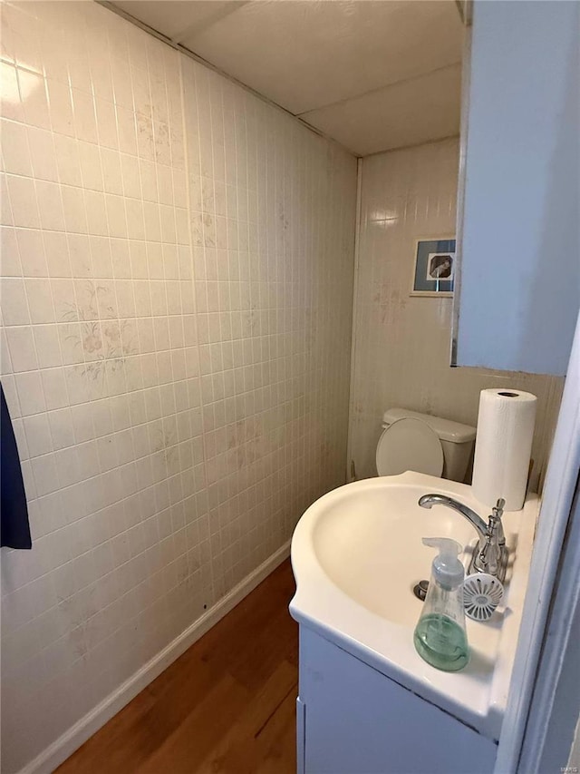 half bath featuring vanity, wood finished floors, toilet, and baseboards