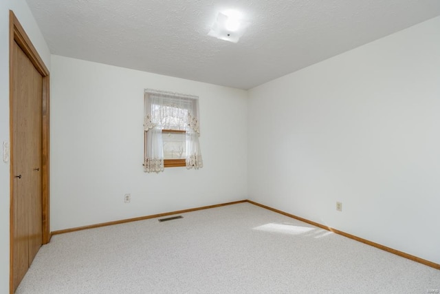 carpeted spare room with visible vents, a textured ceiling, and baseboards