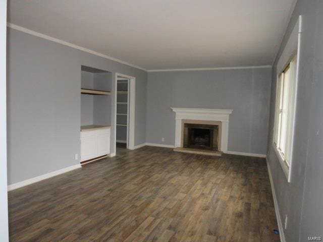 unfurnished living room with dark wood finished floors, a fireplace with raised hearth, crown molding, and baseboards