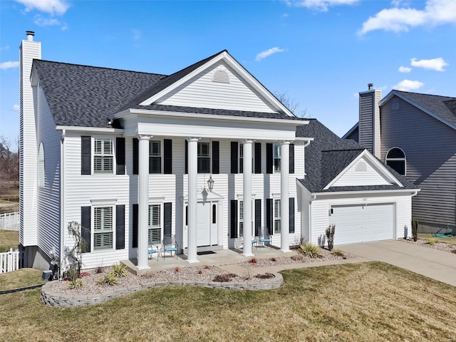 neoclassical / greek revival house with an attached garage, a front lawn, roof with shingles, a chimney, and driveway