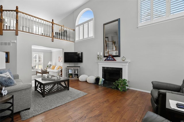 living area featuring visible vents, wood-type flooring, a premium fireplace, baseboards, and a towering ceiling