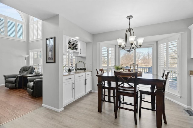 dining space with light wood-style flooring, a notable chandelier, baseboards, and visible vents