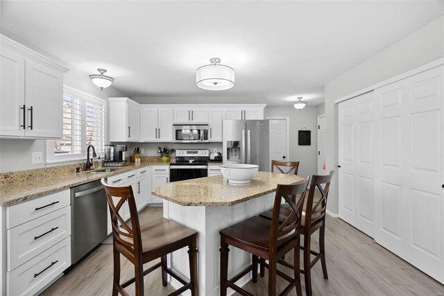 kitchen with light wood-type flooring, appliances with stainless steel finishes, a kitchen breakfast bar, white cabinetry, and a sink