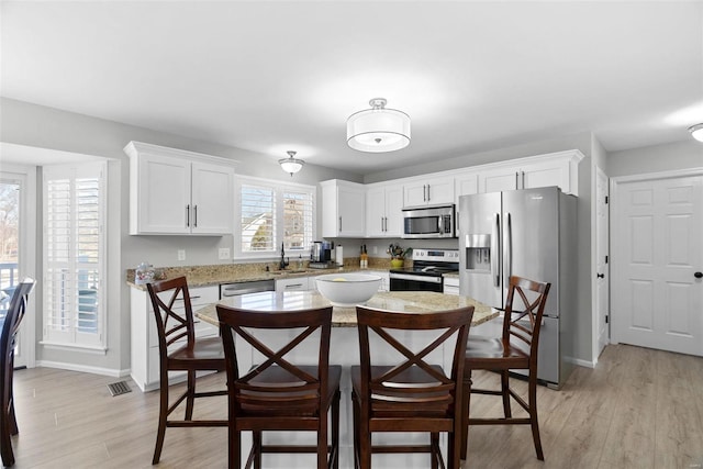 kitchen featuring white cabinets, a kitchen breakfast bar, stainless steel appliances, and light wood-style floors