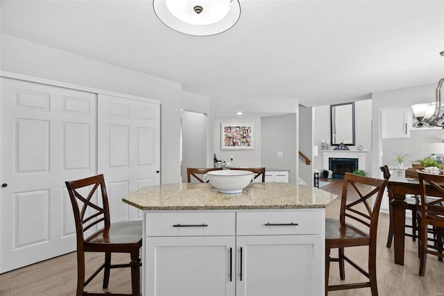 kitchen featuring a kitchen island, light wood-style floors, white cabinets, a fireplace, and light stone countertops