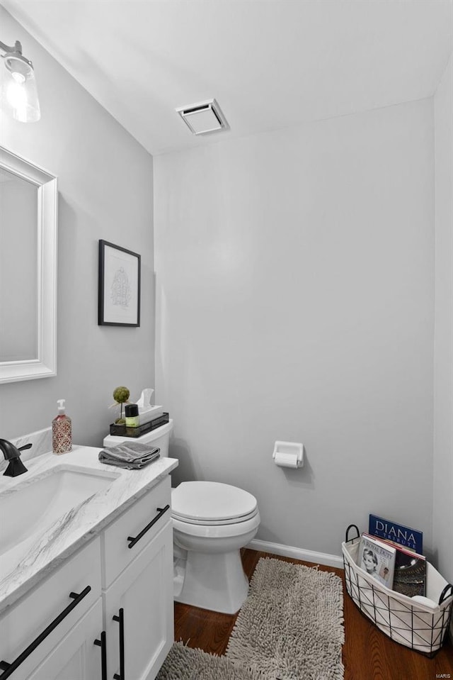 bathroom featuring visible vents, baseboards, toilet, wood finished floors, and vanity