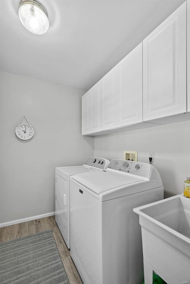 laundry room with light wood-style flooring, a sink, cabinet space, baseboards, and washing machine and clothes dryer