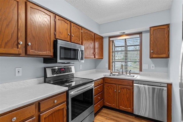 kitchen with brown cabinets, stainless steel appliances, light countertops, a sink, and a textured ceiling