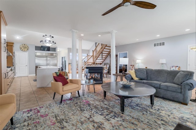 living area featuring visible vents, a ceiling fan, light tile patterned flooring, ornate columns, and stairs