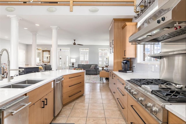 kitchen with open floor plan, ornate columns, stainless steel appliances, under cabinet range hood, and a sink