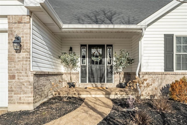 property entrance featuring a garage, covered porch, brick siding, and a shingled roof