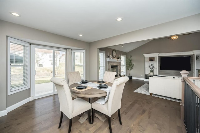 dining room featuring baseboards, a glass covered fireplace, lofted ceiling, dark wood-type flooring, and recessed lighting