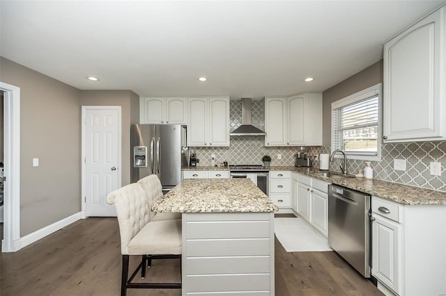 kitchen featuring appliances with stainless steel finishes, a sink, light stone counters, and wall chimney exhaust hood