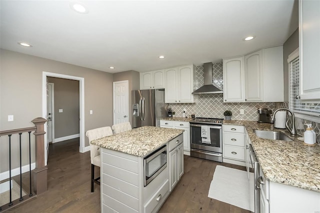 kitchen featuring stainless steel appliances, a sink, a kitchen breakfast bar, light stone countertops, and wall chimney exhaust hood