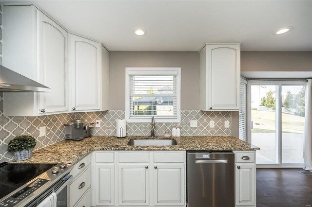 kitchen with wall chimney exhaust hood, appliances with stainless steel finishes, stone counters, white cabinetry, and a sink