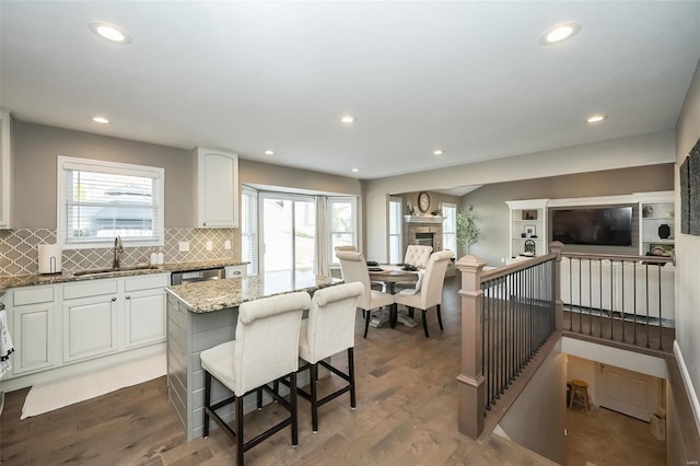 kitchen with light stone counters, a fireplace, wood finished floors, a sink, and a healthy amount of sunlight