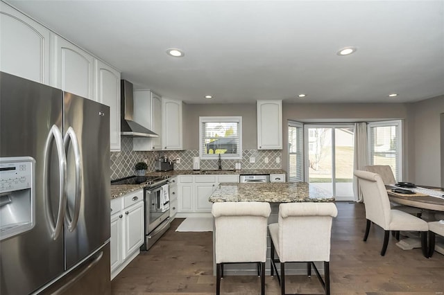 kitchen featuring dark wood-style flooring, stone counters, stainless steel appliances, wall chimney range hood, and a sink